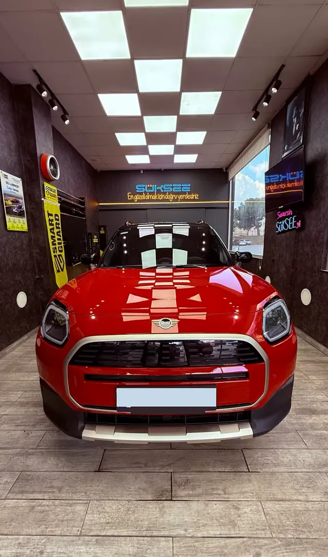 Süksee'de işlem sonrası kırmızı Mini Countryman; arkada mavi neon Süksee tabelası ve Smart Guard afişi
